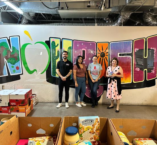 four individuals posing in front of nourishphx mural for volunteer commitment continues blog post
