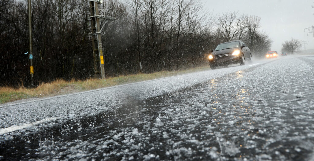 road blanketed in hailstones during a hailstorm, with two cars driving through the icy scene