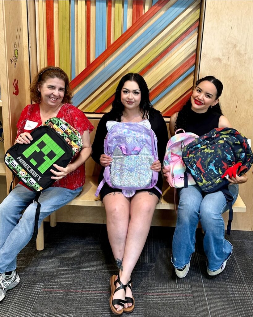 three volunteers at foster alliance pose with backpacks