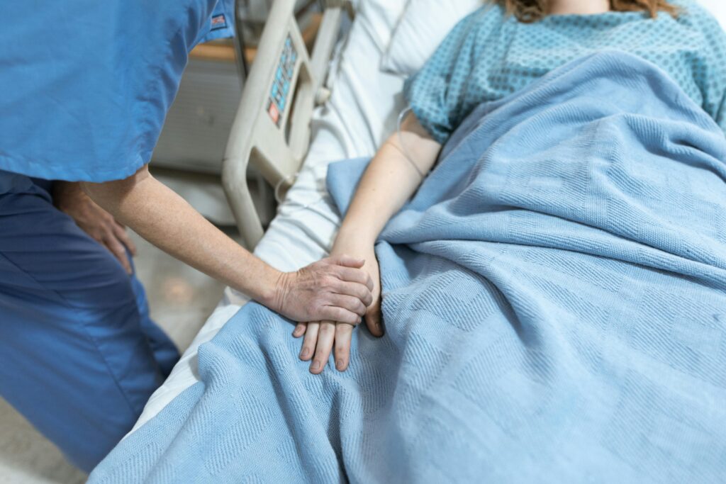 image of patient under blanket with doctor holding hand for What Are Bair Hugger Warming Blankets Used For blog post