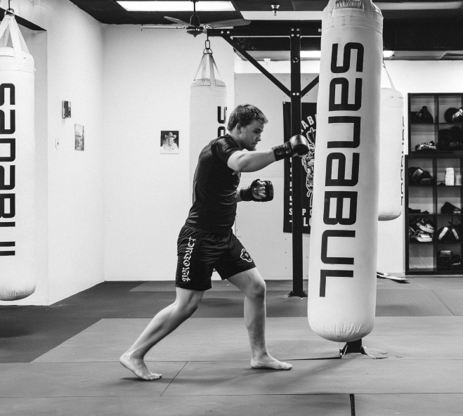barefoot man with boxing gloves, hitting a punching bag in gymnasium