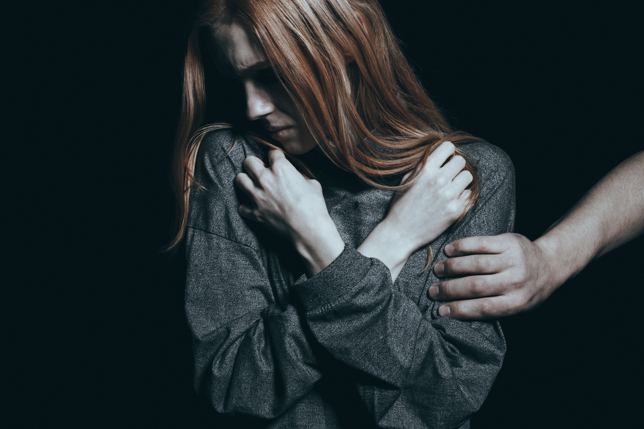 sad woman with arms crossed over her chest and a man's hand on her arm