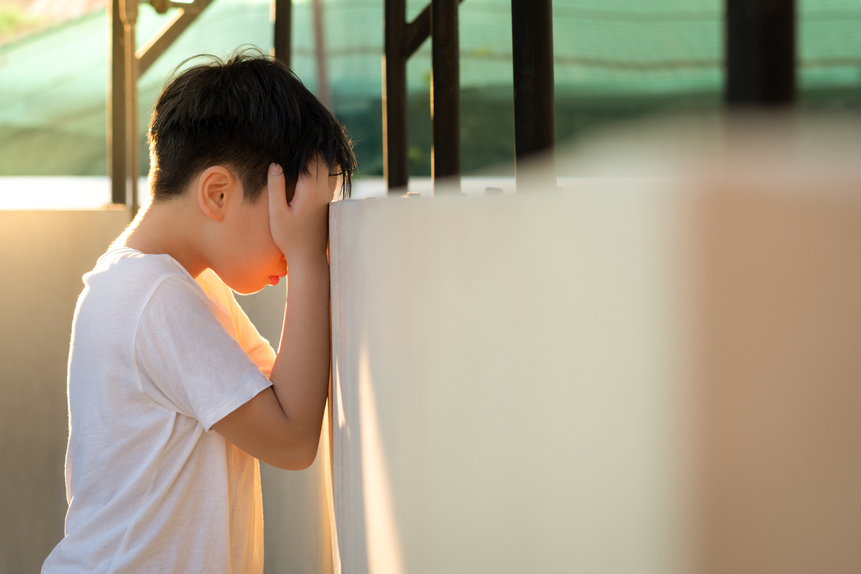 Asian preteen boy standing and leaning head against wall at home, hand cover face, feeling depressed and frustrated.