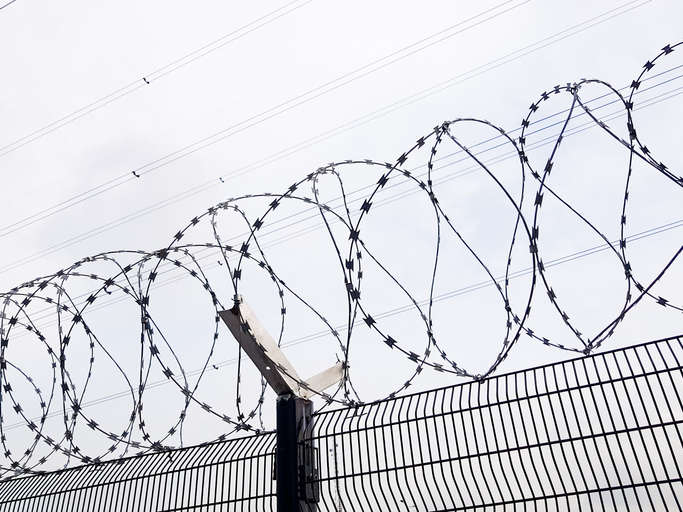 Razor wire coils on top a wire mesh fence. Confinement, prison and border security concept.