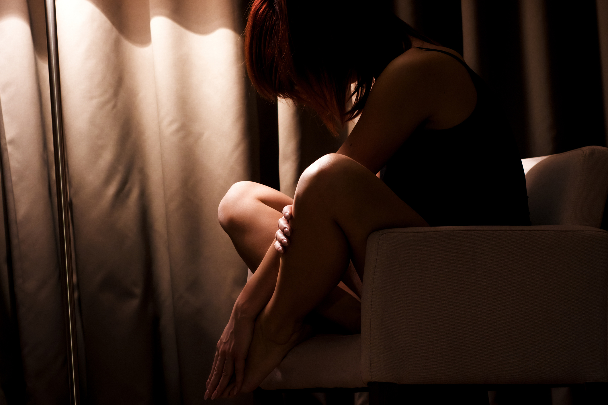 Portrait of a woman in underwear sitting on a chair illuminated only with ambient light of the lamp.
