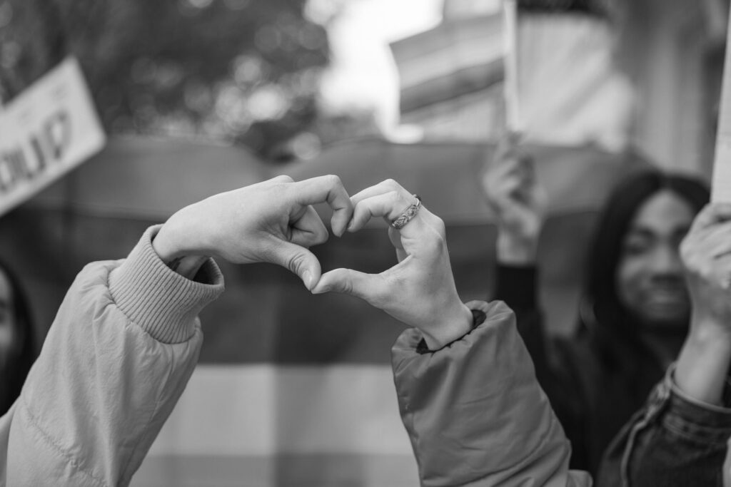 image of hands making a heart sign in front of a pride flag for pride month blog